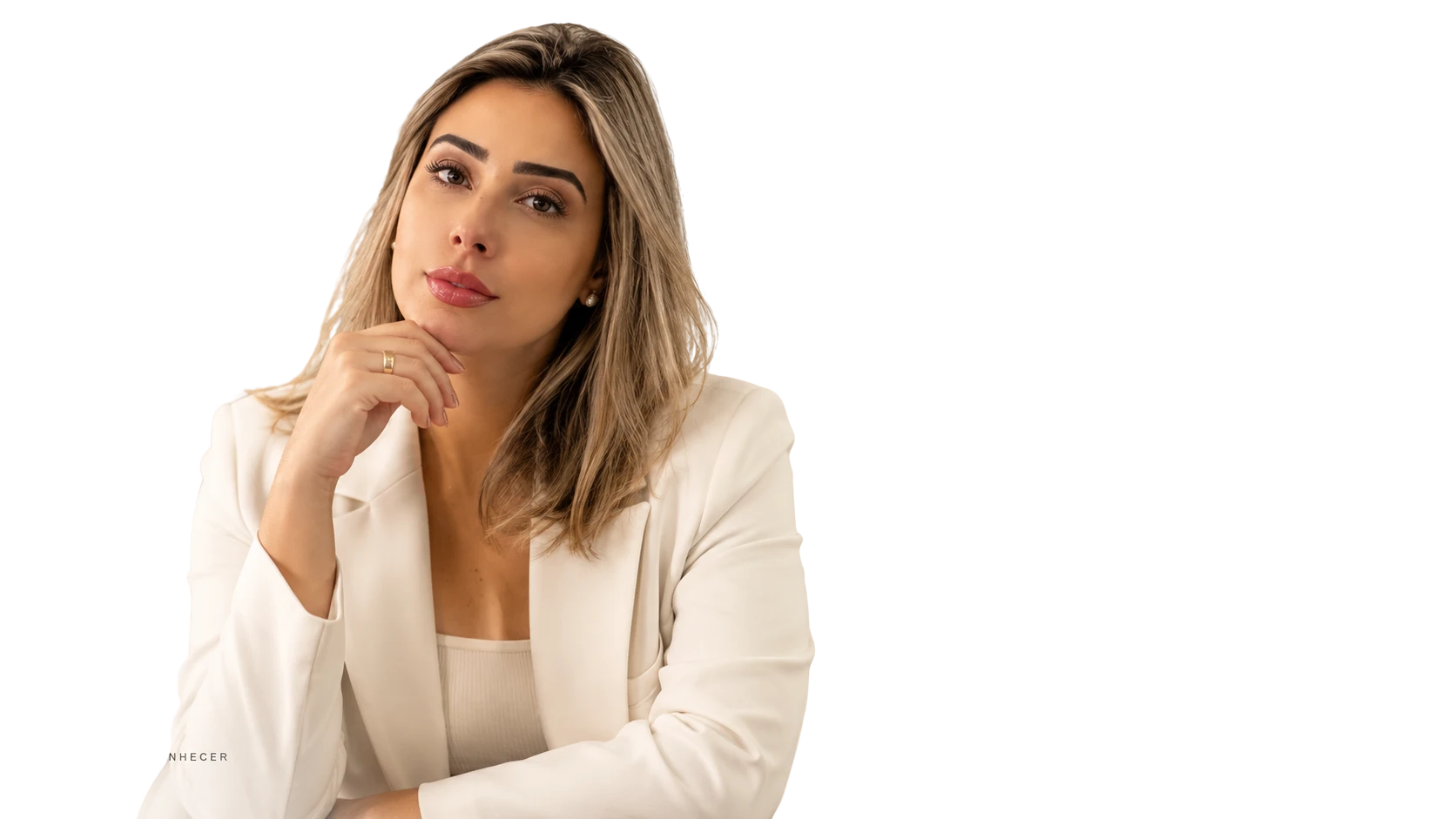 Amanda Morais, sentada com a mão apoiada no queixo, vestindo blazer branco